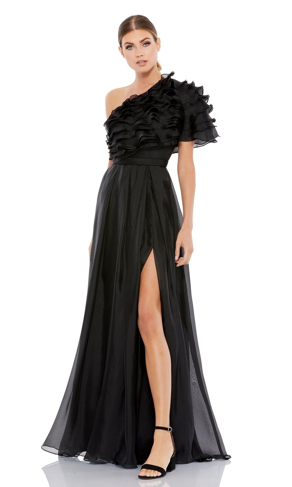 A woman wears the Mac Duggal 26527, a one-shoulder black formal dress with ruffles, a high waist, and a thigh-high slit, stylishly paired with black high-heeled sandals.